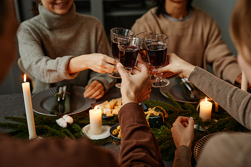 Close up of four friends enjoying Christmas dinner together and toasting with wine glasses while sitting by elegant dining table with candles