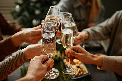 Close up of friends clinking champagne glasses while enjoying Christmas dinner together sitting by elegant dining table with candles