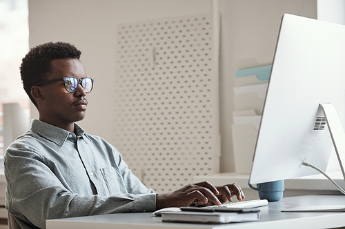 Minimal side view portrait of young African-American man using computer and writing code in software development office, copy space