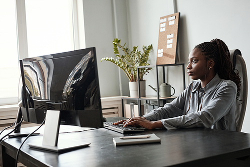 Side view portrait of successful African-American woman using computer while sitting at desk in office, female CEO concept, copy space