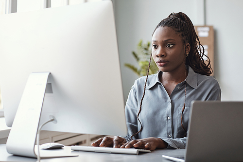 Portrait of young African-American woman using computer and writing code while working in software development office, copy space