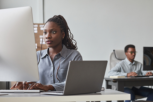 Portrait of two African-American young people using computers while working in software development office, copy space