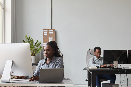 Wide angle portrait of two African-American young people using computers while working in software development office, copy space
