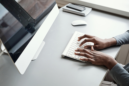 Minimal close up of unrecognizable African-American woman using computer while working at desk background, focus on hands typing at keyboard, copy space