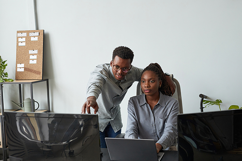 Front view portrait of two African-American young people collaborating on project while using computer together in office, copy space