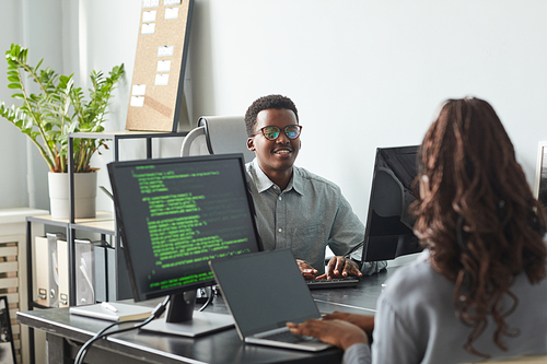 Portrait of smiling African-American man talking to colleague across table while working together in software development office, copy space