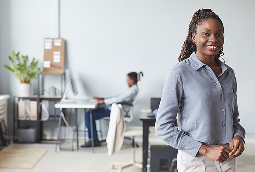 Waist up portrait of successful African-American woman smiling at camera while posing in office interior, copy space