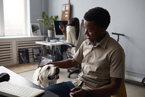 Portrait of smiling African-American man petting dog while working in office, pet friendly workspace