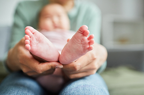 Close-up of young mother holding the little feet of her baby while she lying on her knees