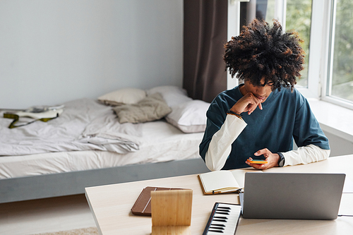 Minimal high angle portrait of African-American teenage boy using laptop while studying at home or in college dorm, copy space