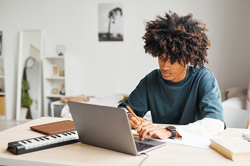 Portrait of male African-American student using laptop while doing homework in college dorm, copy space