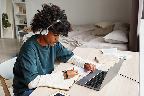 Portrait of African-American teenage boy studying at home or in college dorm and using laptop, copy space