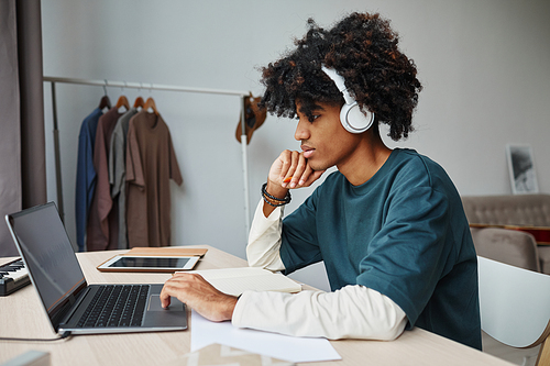 Side view portrait of male African-American teenager studying at home and using laptop