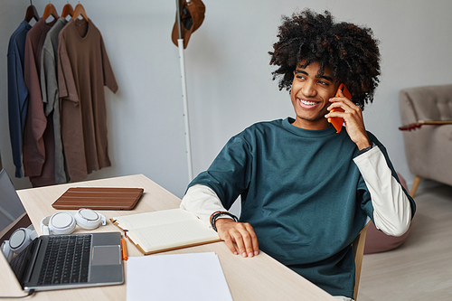 Portrait of smiling African-American teenager speaking by smartphone while studying at home