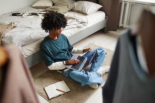 High angle portrait of teenage African-American student sitting on floor at home or in college dorm and studying , copy space