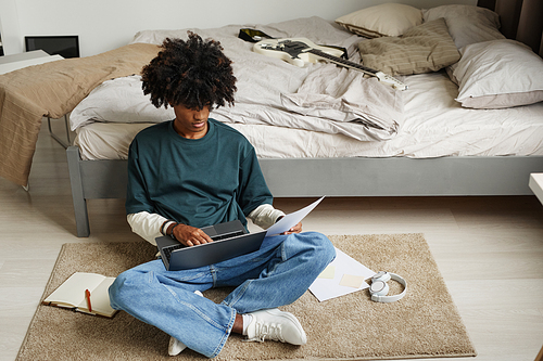 Portrait of teenage African-American student sitting on floor at home or in college dorm and studying , copy space