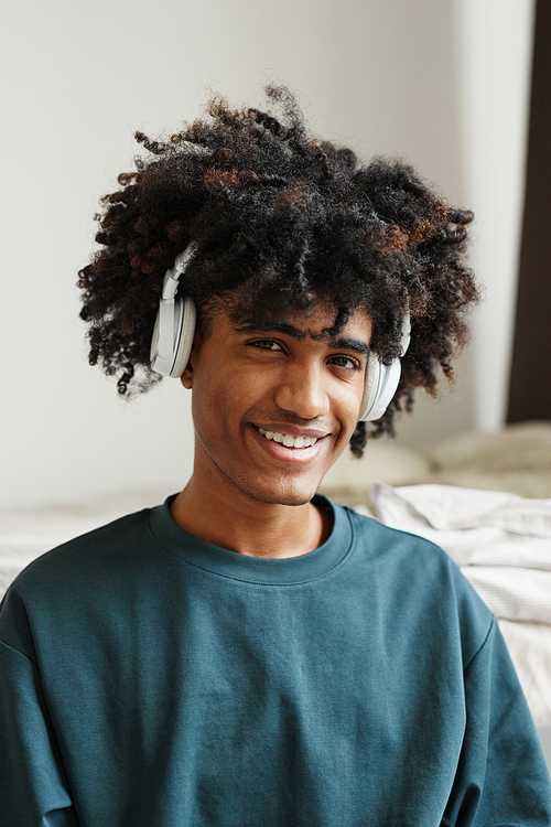 Vertical portrait of smiling African-American teenager wearing headphones indoors with focus on natural hair