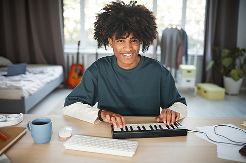 Front view portrait of smiling African-American teenager using electric synthesizer POV shot, copy space