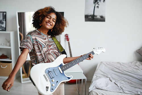 Waist up portrait of smiling African-American teenage girl playing electric guitar at home, copy space