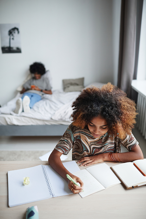 Vertical portrait of female student doing homework and writing in notebook copy space