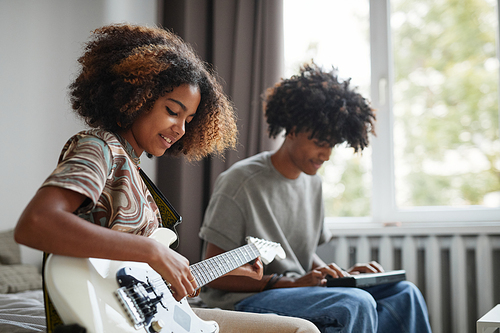 Side view portrait of two African-American teenagers playing electric guitars at home and smiling happily, brother and sister concept, copy space