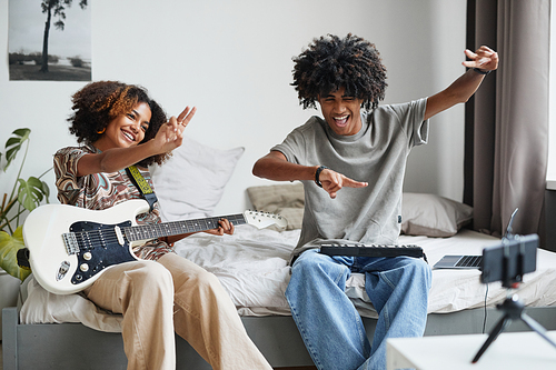 Portrait of two African-American teenagers playing music at home and recording video or livestream, brother and sister concept, copy space