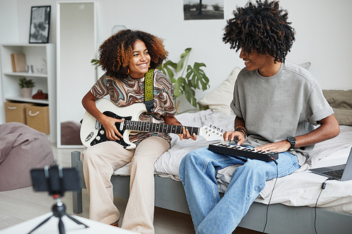 Portrait of two African-American young people playing music at home and recording video or livestream, brother and sister concept, copy space