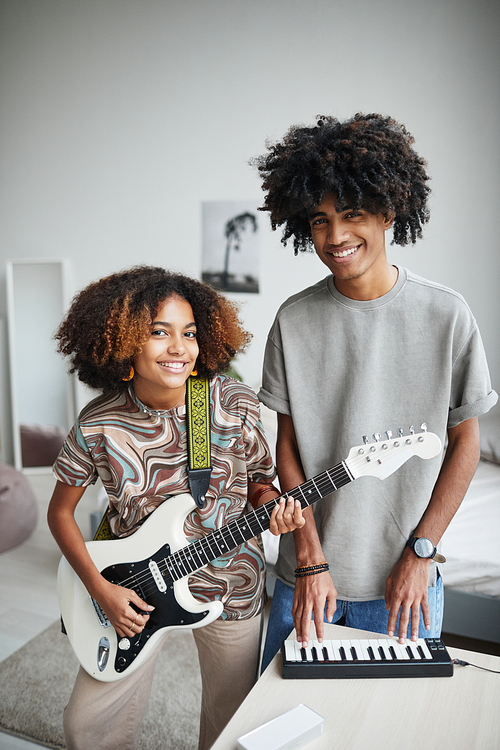 Vertical portrait of two African-American young people playing music at home and smiling at camera, brother and sister