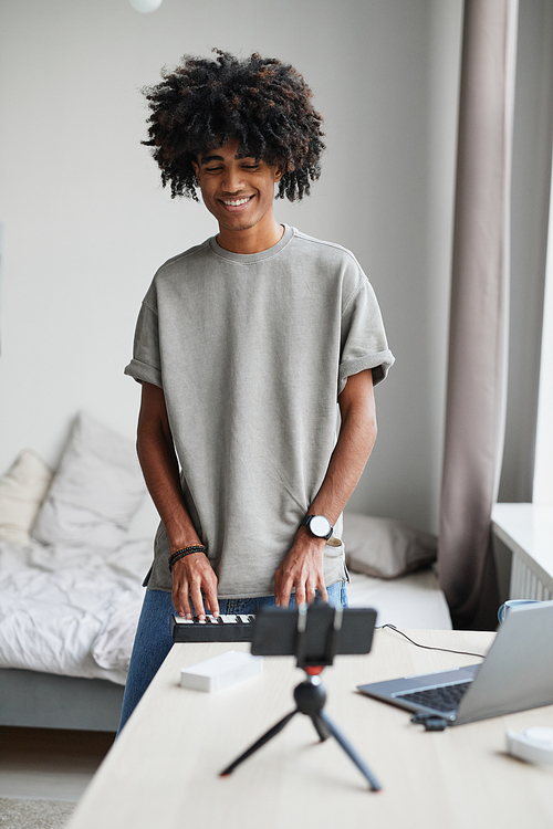 Vertical portrait of young African-American man playing music at home and recording video or livestream