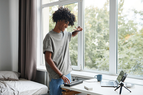 Portrait of young African-American man playing music at home and recording video or livestream, copy space