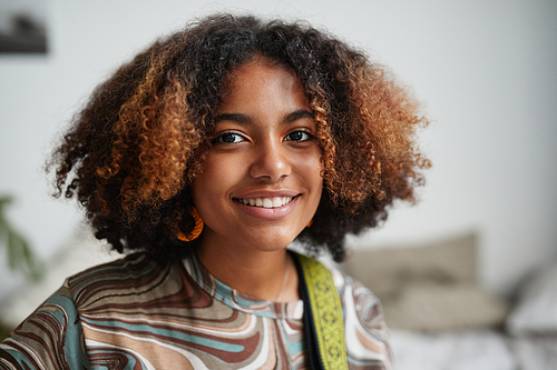 Close up portrait of teenage African-American girl smiling at camera indoors with focus on curly natural hair, copy space