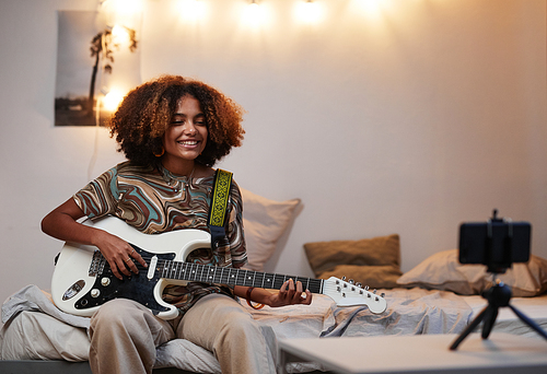 Portrait of young African-American woman playing guitar at home and recording video or livestream,copy space