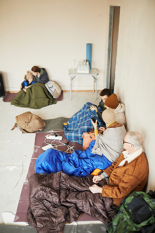 High angle view at group of refugees in camp shelter sitting on floor mats with sleeping bags