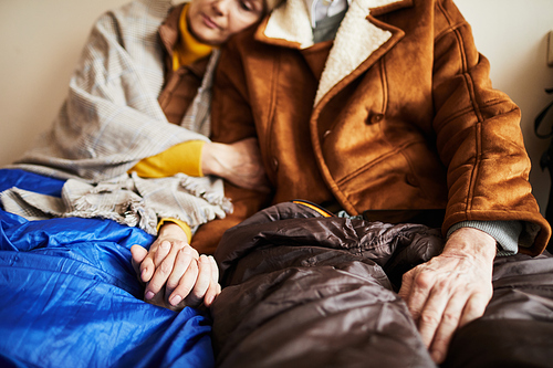 Close up of senior refugee couple hiding in shelter and holding hands in hope during war or crisis, copy space