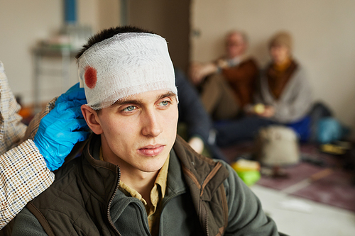 Close up of nurse bandaging head of wounded civilian man in refugee shelter, copy space