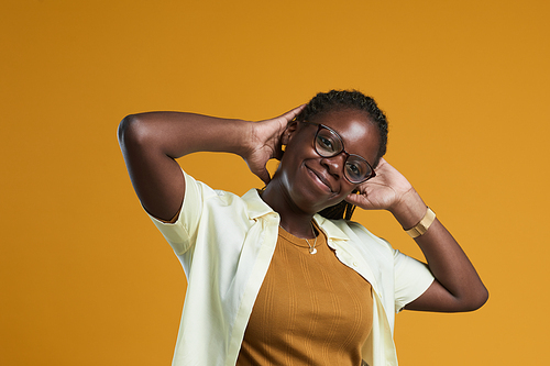 Portrait of carefree African-American woman looking at camera and smiling while posing against yellow background in studio, copy space