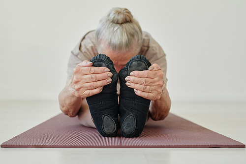 Senior active female holding her feet while bending forwards and keeping head on stretched legs while performing yoga asana