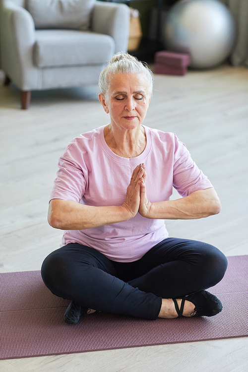 Tranquil senior sportswoman in leggins and t-shirt sitting in lotus position on yoga mat, relaxing and meditating at leisure