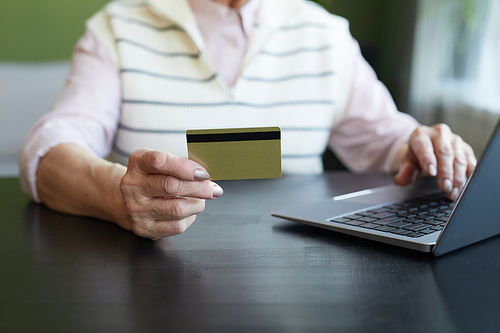 Hand of contemporary elderly woman with credit card sitting by table in front of laptop and shopping online at home