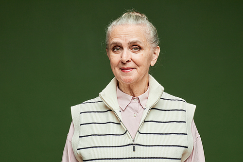 Happy grey-haired senior woman in striped casual clothes looking at camera while standing on dark green background