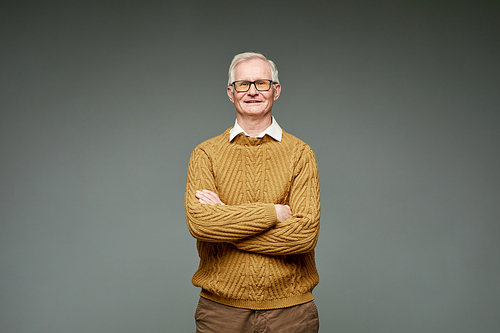 Contemporary aged grey-haired businessman in knitted brown sweater keeping crossed arms by his chest and looking at camera