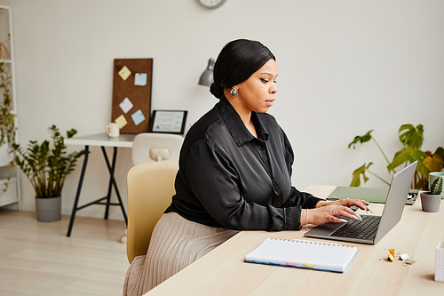 Side view portrait of black young businesswoman using laptop at desk in minimal office interior, copy space