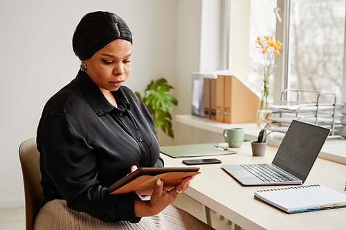 Portrait of elegant black businesswoman using tablet at desk in minimal office interior, copy space