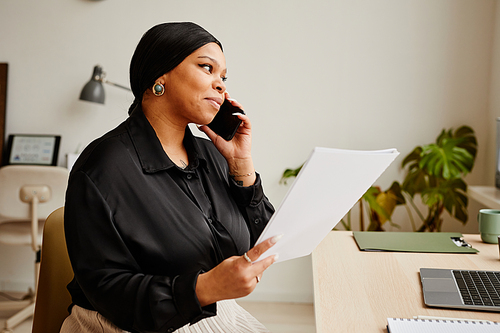 Portrait of elegant black businesswoman calling by smartphone at workplace in minimal office interior, copy space