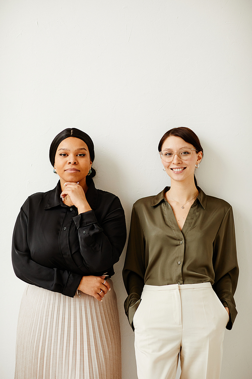 Vertical portrait of two young businesswomen smiling with joy while standing against neutral background