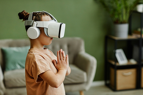 Side view portrait of tween girl practicing yoga workout in VR at home against green wall, copy space