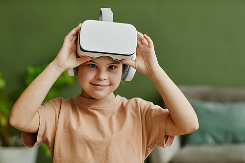 Waist up portrait of cute girl with down syndrome enjoying VR at home and looking at camera, copy space