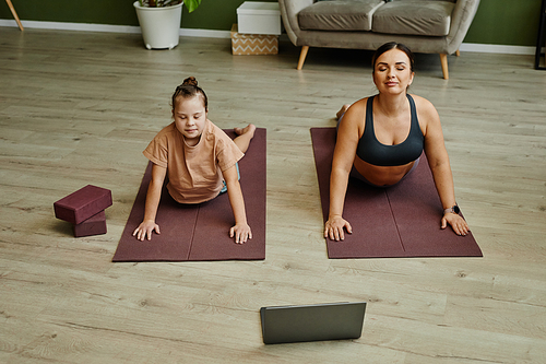 High angle view at mother and daughter with down syndrome working out together at home and doing stretching exercises on mats