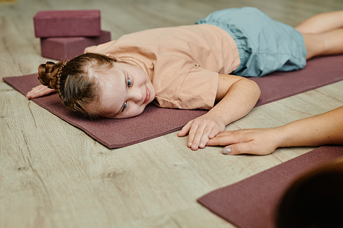 Portrait of young girl with down syndrome lying on exercise man at home and holding hands with mother or instructor helping