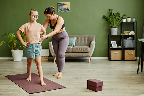 Full length portrait of young girl with down syndrome exercising indoors with female instructor assisting, copy space